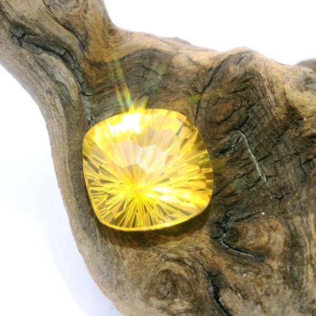 A brilliant cushion-cut yellow gemstone with radiant facets resting on a piece of textured natural driftwood.
